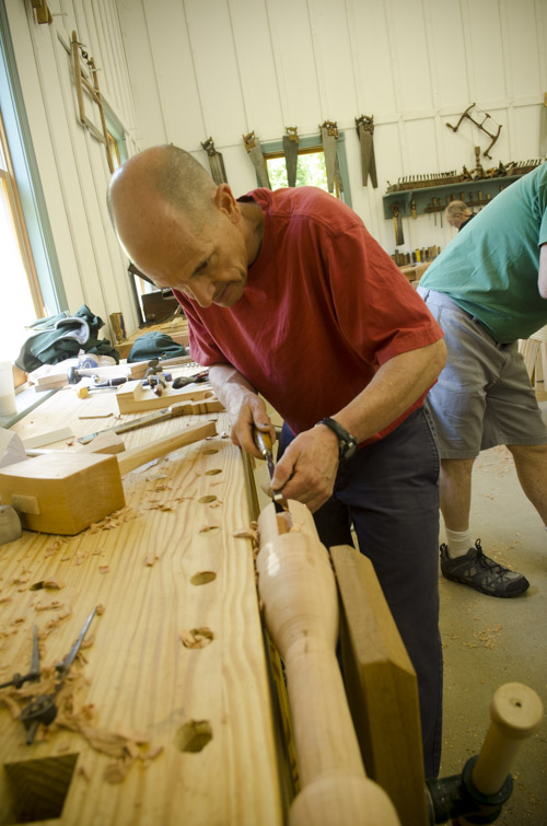 a male woodworking student using a chisel to cut a sliding dovetail joint on a table spindle at his workbench at Joshua Farnsworth's Wood And Shop Traditional Woodworking School