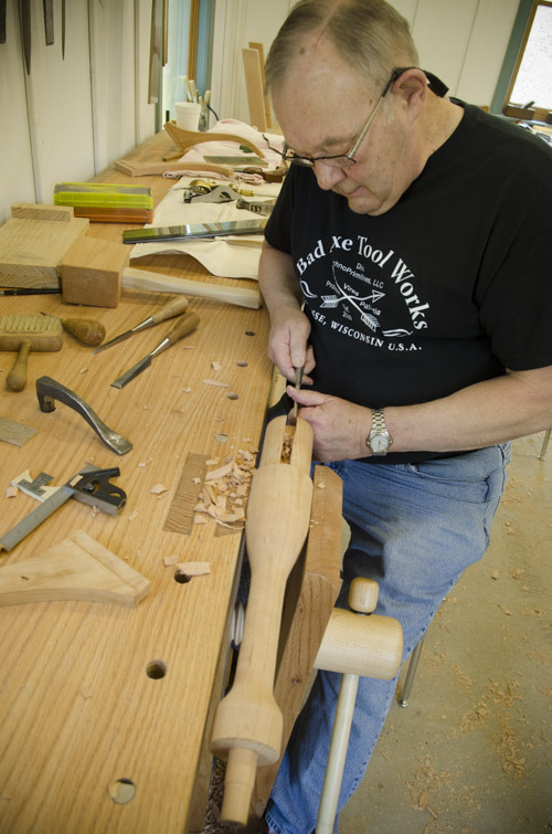 a male woodworking student using a chisel to cut a sliding dovetail joint on a table spindle at his roubo workbench at Joshua Farnsworth's Wood And Shop Traditional Woodworking School