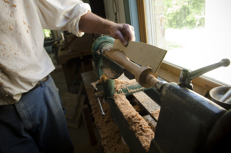 Will Myers holding a pattern to a spindle while woodturning at Joshua Farnsworth's Wood And Shop Traditional Woodworking School