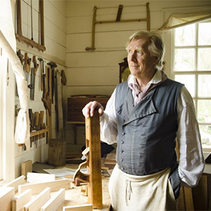 Kaare Loftheim standing with a hand planer next to a wooworking workbench at the Anthony Hay Cabinetmakers Shop at Colonial Williamsburg