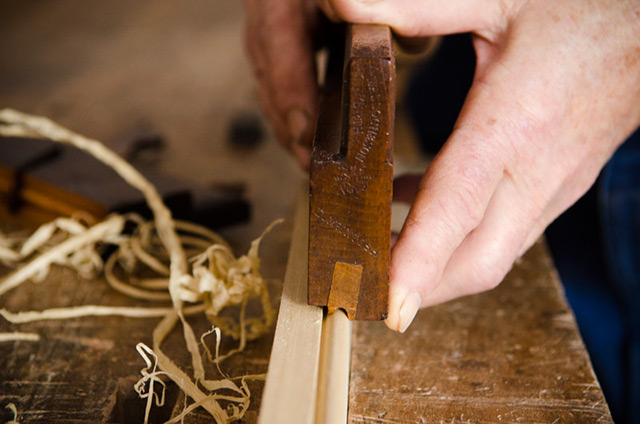 woodworker holding a beading plane to cut a bead on a board