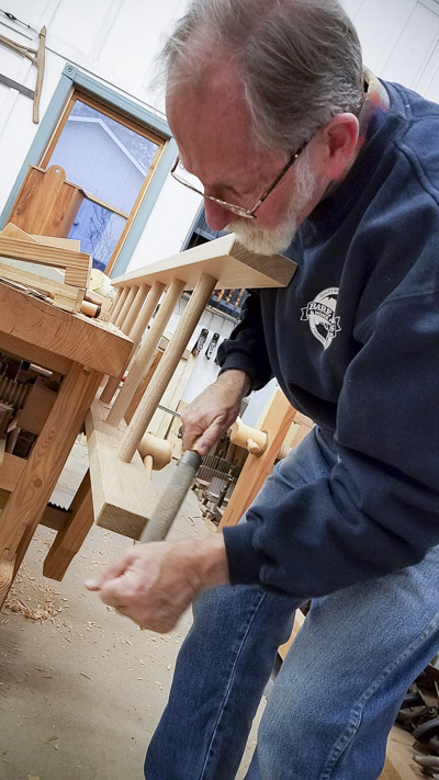 Older man using a rasp to make a bevel on a ladder in a ladder making class